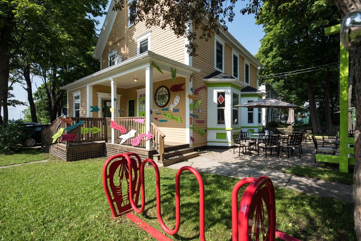 Yellow Victorian house with bright lime-green pergola and pink patio umbrellas