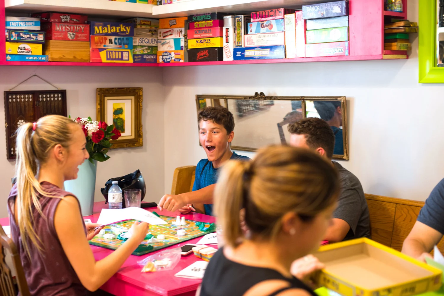 Teenagers laughing around a board game at a hot-pink table